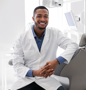 Young male dentist smiling while leaning on dental chair