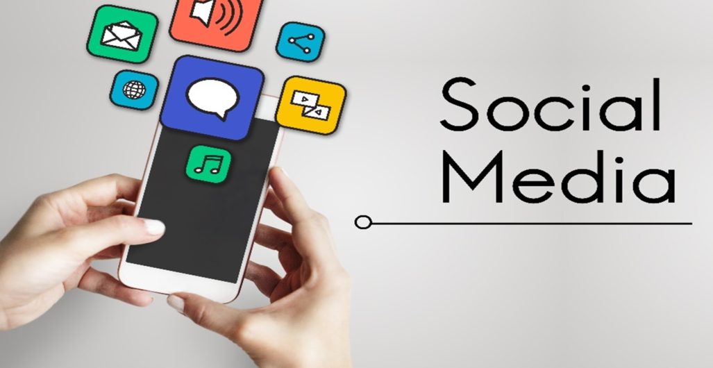 Two hands holding a phone with several icons popping off of the screen with “social media” written next to it.