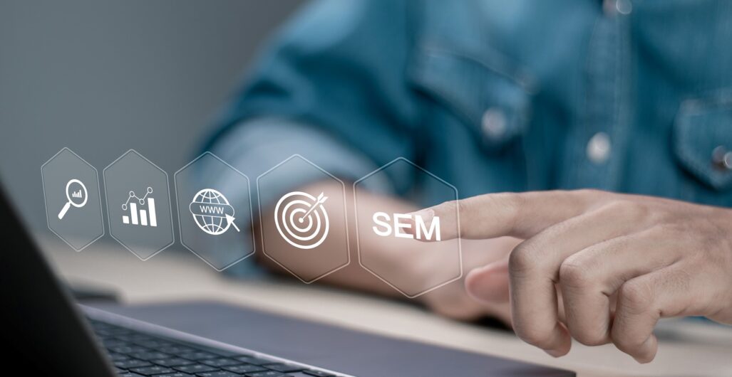 A person’s torso in front of a laptop with digital marketing icons in the air and they are touching the one that says “SEM.”