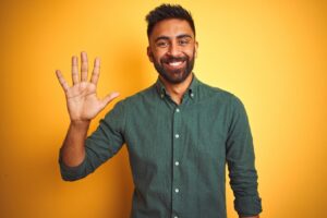 A smiling man wearing a green button-down shirt while holding up the five fingers of one hand. 