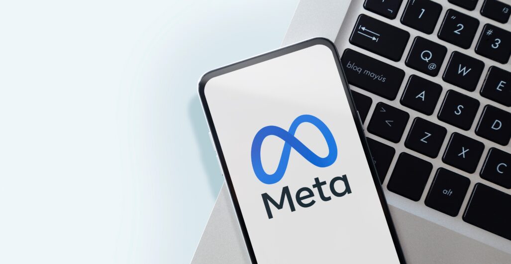 A phone with the Meta logo on the screen on top of the edge of a laptop keyboard.