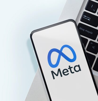 A phone with the Meta logo on the screen on top of the edge of a laptop keyboard.