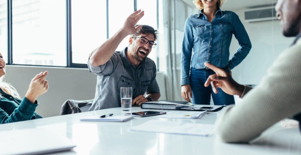 A team of coworkers in a conference room talking and laughing while they develop their brand voice.