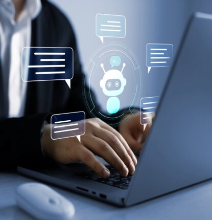 The torso of a person in a button-down dress shirt and sports jacket typing on a laptop with digital graphics showing chat bubbles surrounding a bot icon floating above the hands.
