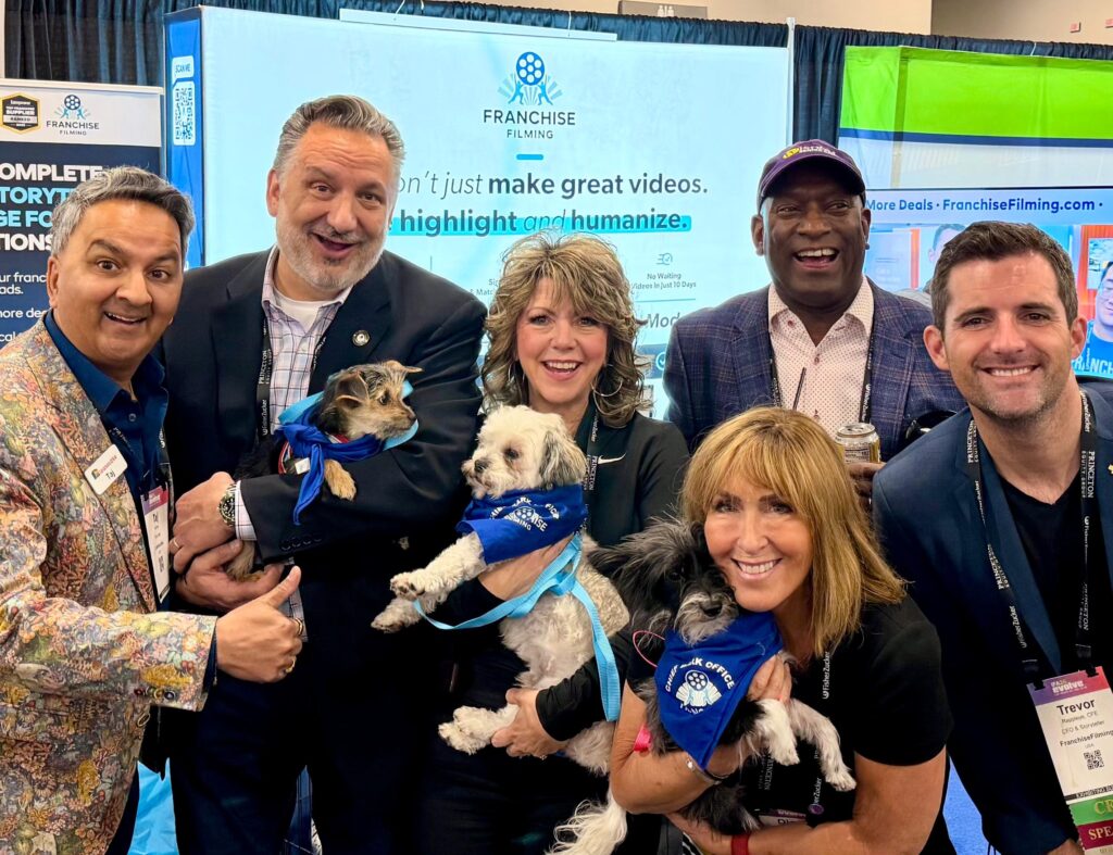 Michele Brevig holding a puppy at the Franchise Filming booth surrounded by other IFA conference members holding puppies. 