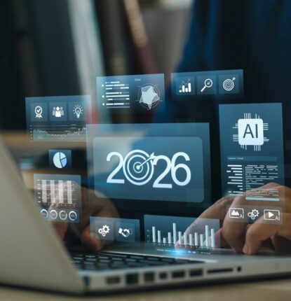 Hands on laptop with holographic dashboards showing 2026, target icon, AI chip, charts, and KPIs, illustrating business goals, growth strategy, data analytics, forecasting, and digital transformation.